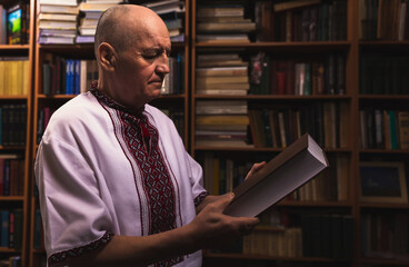 Senior man in folk clothes holding an book at home library