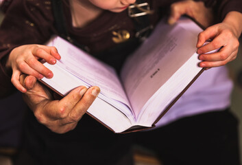 Grandfather and granddaughter read a big book at home library. Close up old hands and kid hands...