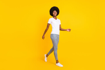 Full length photo of pretty friendly dark skin woman dressed white t-shirt smiling walking isolated yellow color background