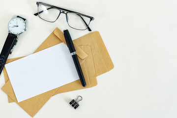 Working place. Blank paper, envelopes, pen, eyeglasses and watch on white desk.