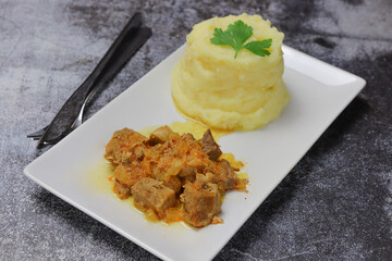 Delicious meat, onion and mashed potatoes on a white plate on a dark concrete background.