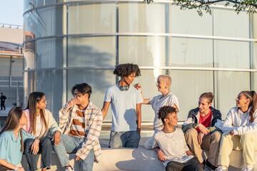 Big group of happy teenage friends talking in a bench in the street of the student campus.