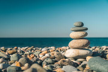 Fototapeta na wymiar Beautiful pyramid of pebbles on the seashore on a sunny day, copy the space. Concept of balance, harmony