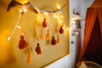 Cozy homemade garland from pompons from threads on the wall in the room, home decor Scandinavian style, mustard and brown, recycling