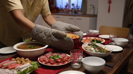 man wearing protective gloves carrying and serving hot soup in pot on the dining table, preparing...