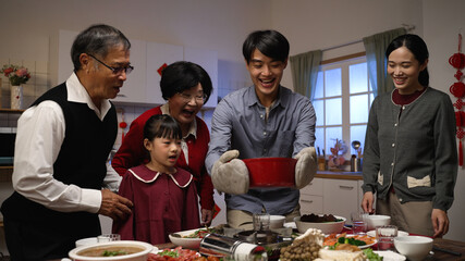 smiling asian father serving hot soup on the dining table and posing with folded arms, feeling...