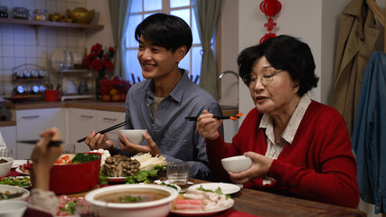 smiling asian adult son giving food to his senior mother as they are having reunion dinner together...