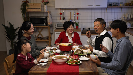 cheerful asian family members having fun chatting and laughing at dining table while enjoying big...