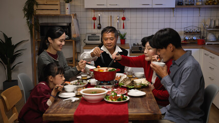 happy asian family members picking food from hot pot with chopsticks while enjoying traditional reunion dinner at home on chinese new year's eve
