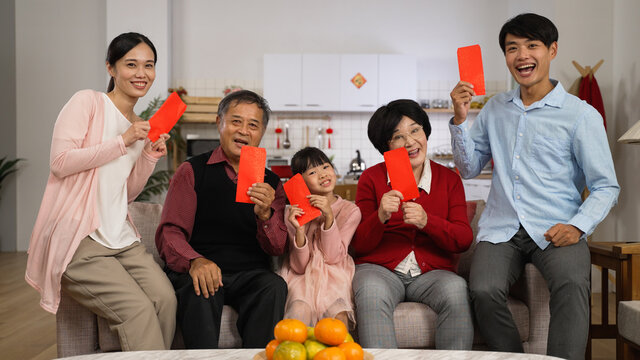cheerful asian extended family looking at camera and making thumb victory hand signs while taking burst shots with lucky money at home on chinese new year