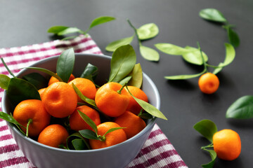 Mandarins or clementines with leaves on a black background. Tangerines in a plate.