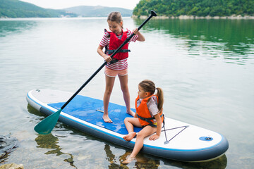 Children in swim life vest swimming on stand up paddle board together. Girls paddleboarding on SUP...