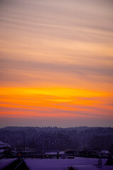 Obraz premium Bright orange sky over a village. Vivid colors of sunset in winter. Colorful vertical cloudscape. Selective focus on the details, blurred background.