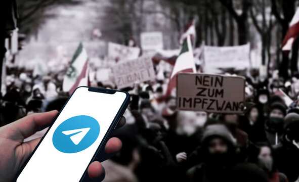 Telegram Logo wird auf einem Smartphone angezeigt, im Hintergrund eine Demonstration von Impfgegnern in der Corona Pandemie, Telegram als Netzwerk von Querdenker und Verschwörungstheoretiker
