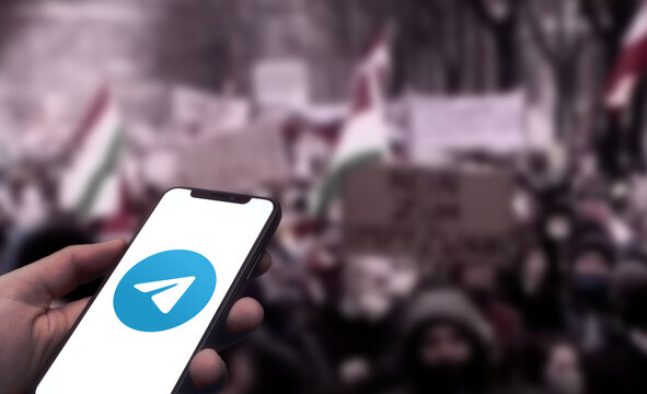 Logo des Messengers Telegram wird auf einem Smartphone angezeigt, im Hintergrund eine Demonstration mit vielen Menschen, Schilder und Fahnen, Hetze, Fake-News, Verschw&ouml;rung, Verbot, Kontrolle