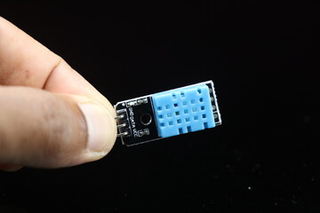 Temperature and humidity sensor module or DHT11 board held in hand isolated on black background