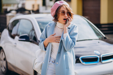 Obraz premium Young woman talking on the phone by her electro car