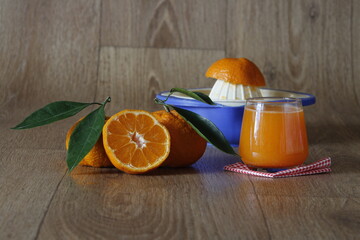 Homemade mandarin or tangerine juice and blue squeezer on wooden texture background. Glass of fruit juice on plaid.
