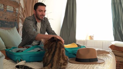 Man packing clothes suitcase in vintage room, getting ready for road trip preparing luggage and petting cat. making travel plans concept. 4k footage