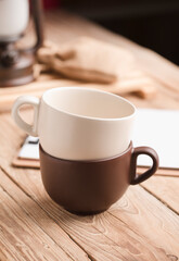 Two cups of coffee or tea stacked on old wooden table, with notebook, raffia sack, lamp