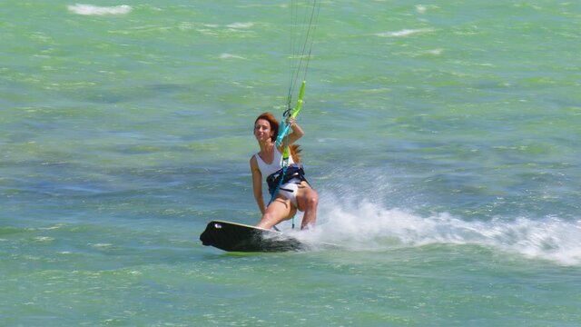 Beautiful girl kitesurfing in white swimsuit. Extreme kiteboarding in slow motion. Summer fun action sports.