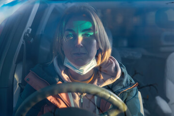 Portrait of a young woman wearing a protective mask sitting at the wheel of car. View through the windshield. New normal concept