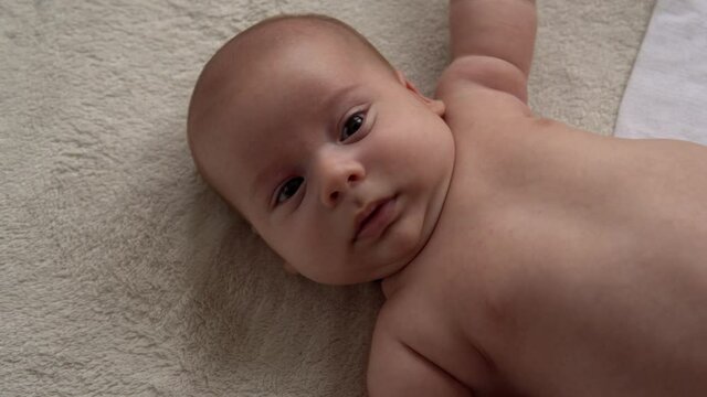 Childhood, motherhood, family, hygiene, infant concept Close-up Happy playful nake kid 2 month newborn boy looking at camera after bath shower on white soft bed. baby child waking time before bedtime