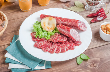 Sliced smoked sausage on a white plate on a wooden background.