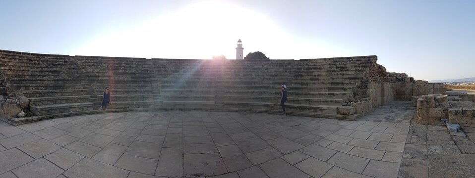 A view on amfiteater in Kato Paphos Archaeological Park, ancient Greek and Roman city in Cyprus. Sun is shining bright. In the back a lighthouse is visible.