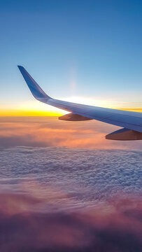 A Colorful Sunrise Seen From The Plane Window. Sun Is Raising From The Clouds, Painting Them Pink And Orange. Horizon Line Turns Yellow With The Sunbeams. Plane Wing Covering The Sun. Romantic View