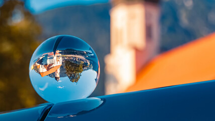 Crystal ball summer landscape shot with reflections on a car roof and a church at Weißenbach am Lech, Tyrol, Austria