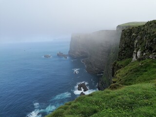 The steep and dramatic cliffs and green mountains off the coast of the Faroe Islands