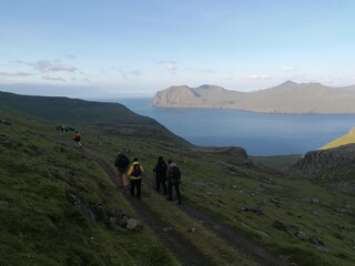 A group of hikers on a green mountain ridge walk in the Faroe Islands