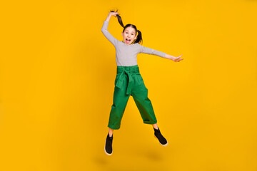 Fototapeta na wymiar Full length photo of young excited school girl jump up hold ponytail isolated over yellow color background