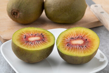 Fresh halved sweet red kiwi on a plate close up and whole ones in the background 