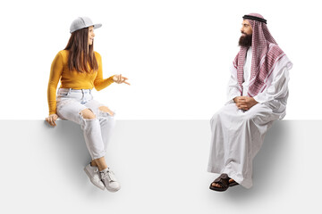 Young casual female and a saudi arab man in traditional clothes sitting on a blank panel and talking
