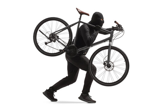 Full length profile shot of a burglar in black clothes with a balaclava stealing a bicycle
