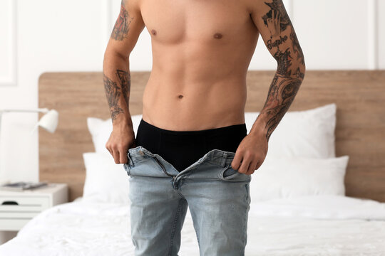 Sexy young man taking off his jeans in bedroom