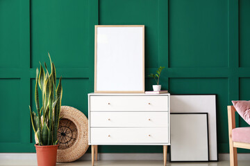 Chest of drawers with blank frame and flowerpot near green wall