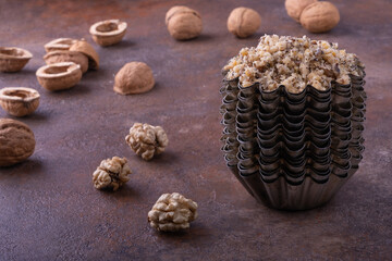 Pounded walnut in a vintage iron baking dish in a pyramid of such forms, next to whole walnut kernels and whole walnuts and empty shells against a blurred background. Selective focus