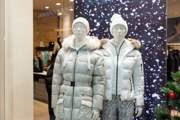 Fototapeta premium Male and female mannequins in stylish winter white clothes in a New Year's shop window.