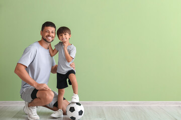 Little boy with soccer ball and trainer near green wall