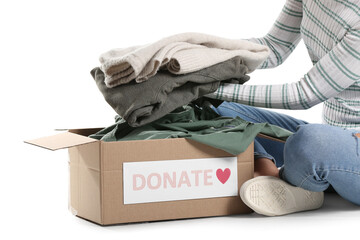 Young woman putting donation clothes in box on white background