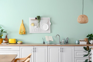 Interior of stylish kitchen with white counters and hanging peg board on green wall
