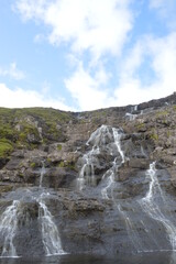 The white streaming waterfalls over the black lava rocks on the Faroe Islands in the Atlantic
