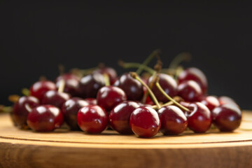 Close up photo of ripe red cherries on wooden plate. Sweet fresh organic cherries. Black background