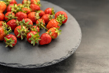 Freshly picked farmers organic strawberries on gray platter. Ripe strawberries with green cuttings.