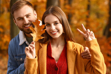Beautiful couple with autumn leaf showing victory gesture in park
