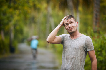 Portrait of drenched young man enjoying heavy rain in nature..