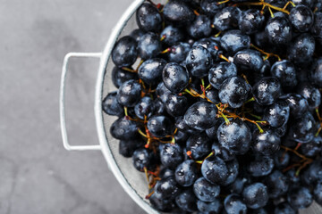 Sweet black grapes in a metal bowl on a dark textured background.
